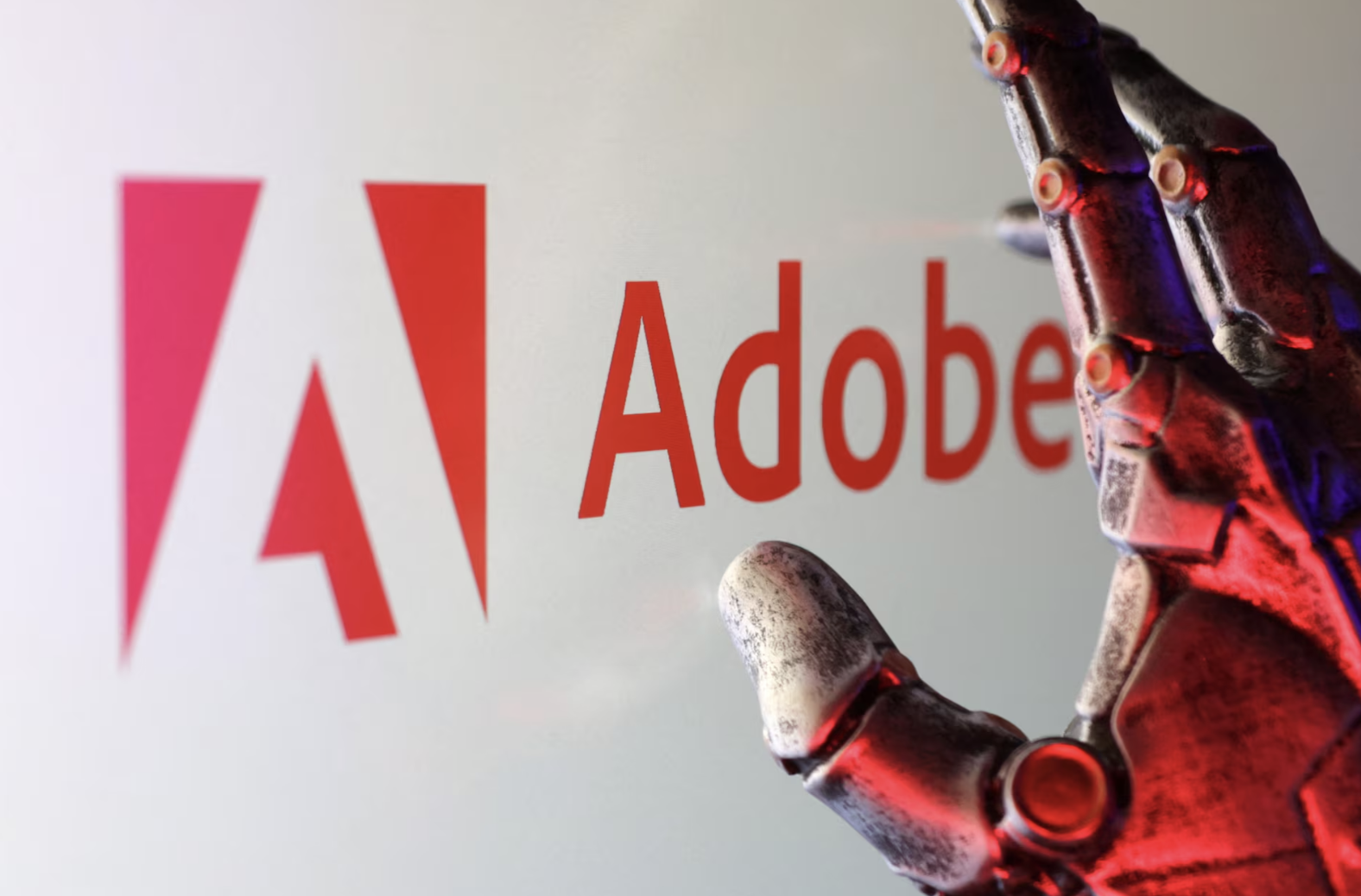 A close-up of a detailed, metallic robotic hand with red and blue lighting, reaching towards the red Adobe logo on a white background.